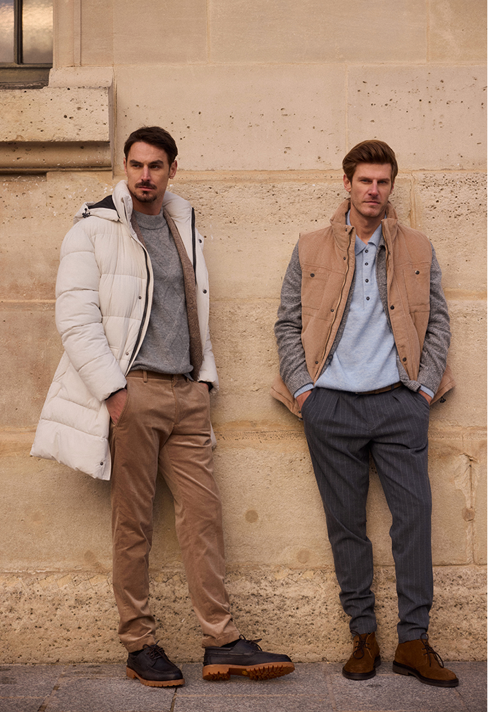 Zwei Herren Herren in Pierre Cardin Looks lehnen an einer Hauswand